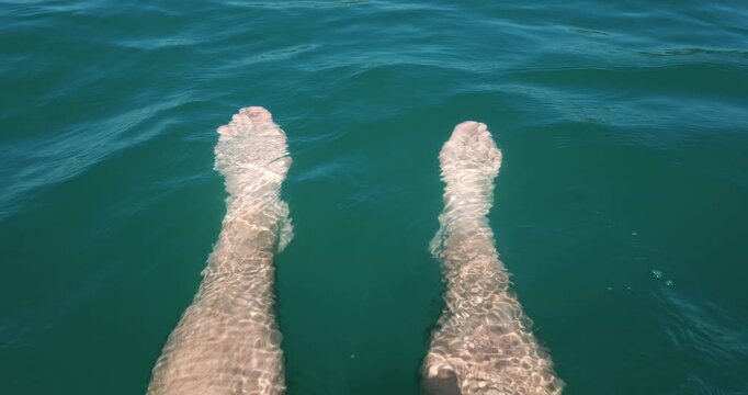 POV of person floating legs and feet in clear turquoise sea water on a sunny day