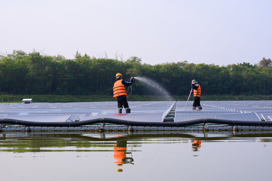 Workers are cleaning solar panels in a large body of water, a clean energy source for electricity generation.