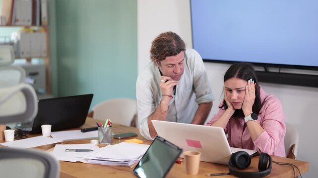Adult man and woman sit together at laptops, sad and tense, solving work problems or facing difficult situation in office