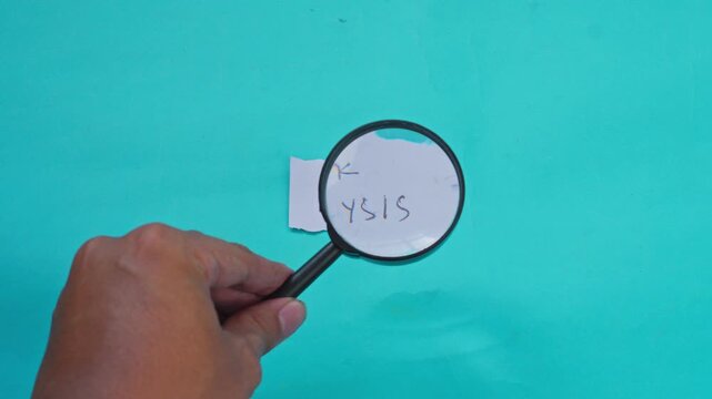 Hand uses magnifying glass to inspect paper note with words RISK ANALYSIS on turquoise background