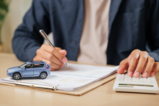A man signs car insurance documents, calculating costs with a loan calculator. Writing his signature on a contract, ensuring smooth financial transactions