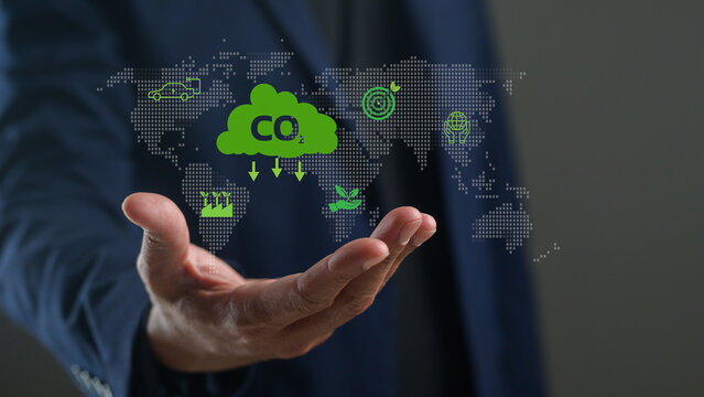 A businessperson holds a digital cloud with CO2 symbols and environmental icons, symbolizing carbon emissions and sustainable technology on a world map.