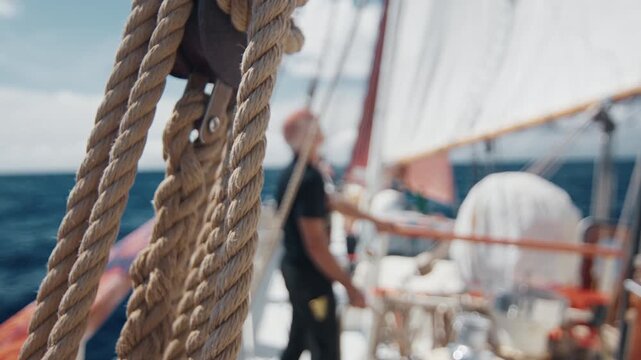 Old captain controls the crew working with the sails on the big expeditional sailing vessel moving in the Atlantic Ocean