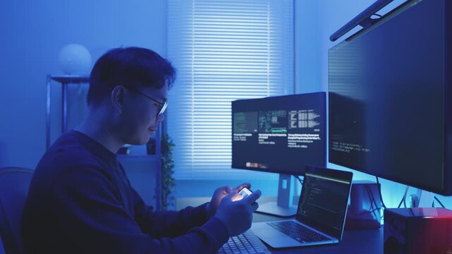 Happy Asia male Software Developer Using Smartphone Relaxing After Finishing Work at Night.
