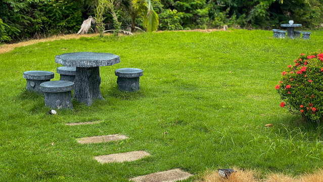 A cozy garden area with a concrete table and stools against a backdrop of green lawn and ornamental plants. The idea is for comfortable relaxation, greenery, and modern landscaping.