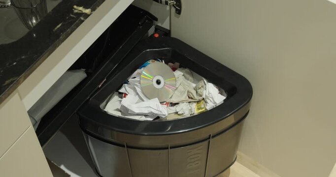 Old compact disc being discarded into a household trash bin, symbolizing obsolete technology, electronic waste, recycling, and digital transformation.