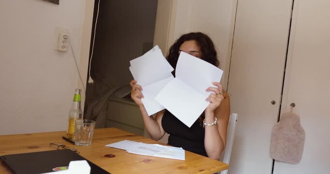 A distressed woman reacts emotionally after opening overdue bills and debt collection letters at home.