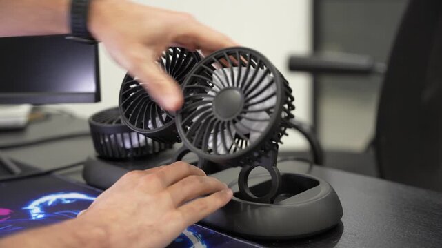 Close-up of a person's hands adjusting a portable triple-head desktop fan on an office desk. This versatile cooling gadget helps improve air circulation and personal comfort in a workspace.
