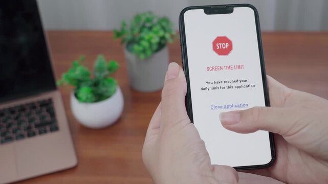 User views a STOP screen time limit AI alert on a smartphone while sitting at a tidy desk with laptop and plants.