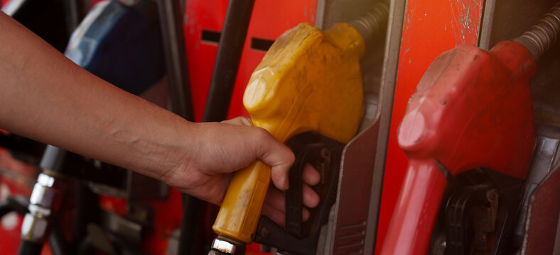A close-up image of a gas station attendant's hand holding a fuel dispenser.	