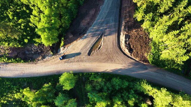 Top-down aerial view of a single blue car parked on a dirt road intersection in a forest