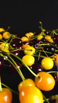 Macro shot of freshly picked ripe yellow and red wild cherries with green stems, showcasing their vibrant colors and juicy texture in a smooth gliding motion against a dark, contrasting background