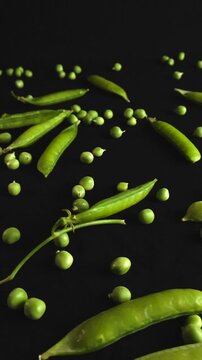Smooth gliding camera movement over fresh green pea pods and scattered peas on a dark background. This detailed macro view highlights the organic texture and vibrant color of the healthy vegetable