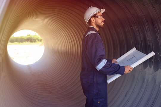 A male engineer in an orange suit is inspecting the integrity and safety of a pipeline.