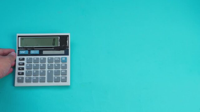 Hand places white calculator on bright turquoise background
