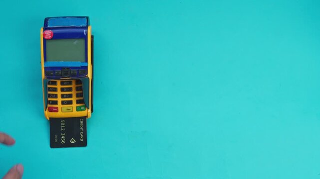 Hand inserts credit card into payment terminal and presses buttons on turquoise background