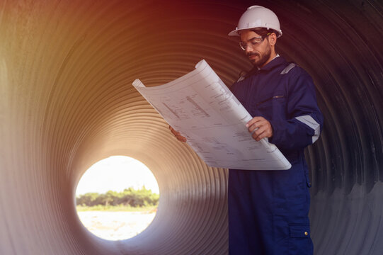 A male engineer in an orange suit is inspecting the integrity and safety of a pipeline.