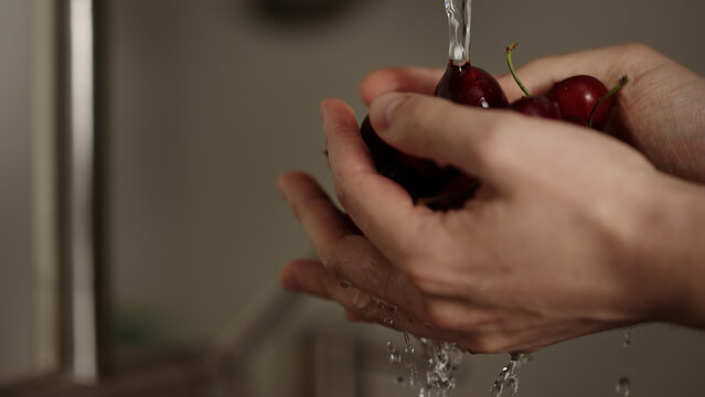 closeup shot of man washing cherries with kitchen faucet