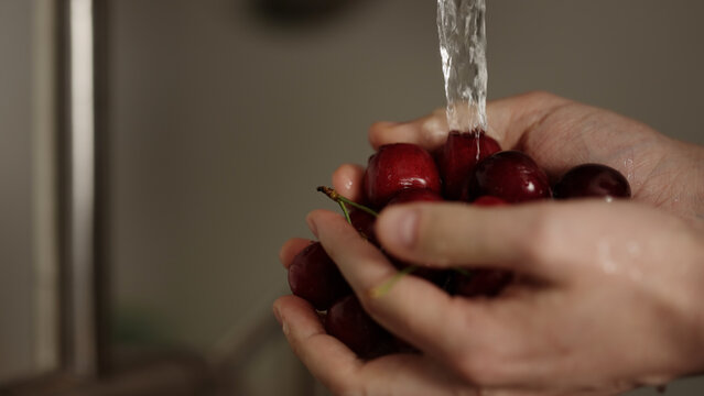 closeup shot of man washing cherries with kitchen faucet