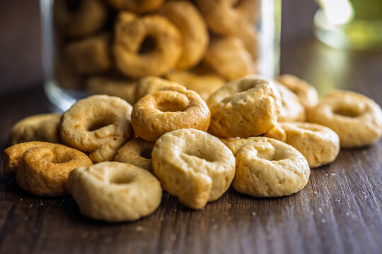 Close-Up of Italian Taralli Cookies Piled on Wooden Table With Glass Jar in Background