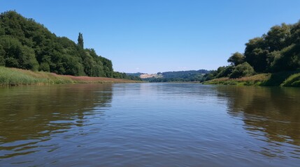 Fototapeta premium Tranquil River Landscape Under Clear Blue Sky Surrounded by Lush Green Trees and Rolling Hills in Scenic Natural Environment