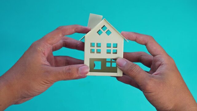 Hands hold miniature house model on turquoise background