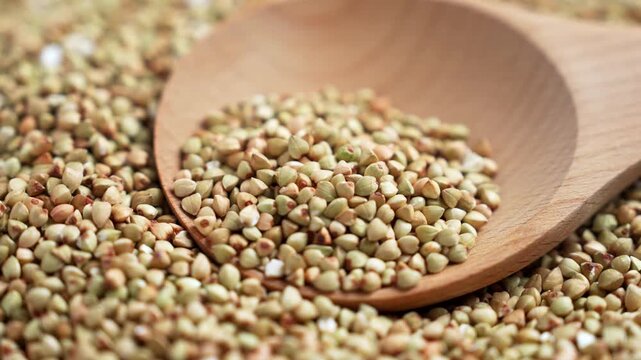 Raw buckwheat groats in wooden spoon on pile of uncooked grains. Healthy gluten free ingredient. Rotation