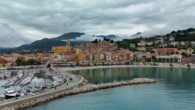 MENTON, FRANCE - NOVEMBER 1, 2025: Panoramic view of Menton harbor and colorful buildings under a cloudy sky