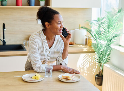 Portrait of a young woman or businesswoman gettyng ready for work preparing and eating breakfast fruit using a smartphone phone standing in kitchen home