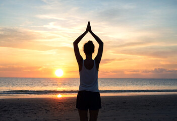 Fototapeta premium Silhouette of a person meditating on the beach during a beautiful sunset over the ocean waves