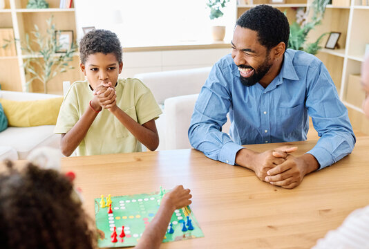 Portrait of a happy african american family at home, having fun playing a board game challenge game, playing board game ludo at home