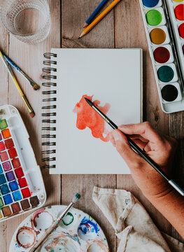 An artist paints a red watercolor wash in a sketchbook