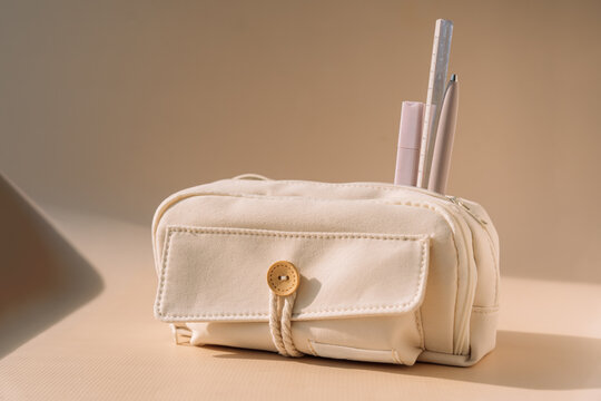 Beige school pencil case with pastel pens on desk in warm natural light.