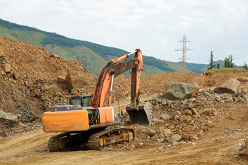 A large excavator is digging on a construction site surrounded by piles of dirt and rocks © Viktoriya