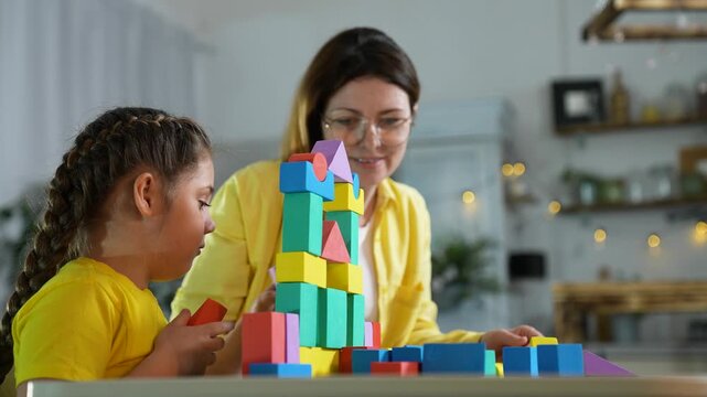 Mother and child play together. Woman and girl build tall tower using colorful wooden block pieces. Mother feels happy watching. Family enjoys indoor activity. Child looks calm holding block.