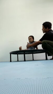 Father assisting a toodler during a physical therapy session on a mini trampoline