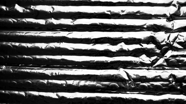 Abstract texture of flexible plastic packaging with reflective foil coating featuring wrinkled metallic surface. Rotation