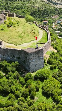 Aerial view of person waving red flag on ancient castle fortress walls at sunset.