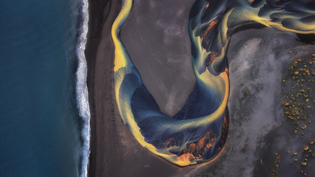 Aerial view of a glacial river delta with intricate sediment patterns flowing into the ocean across black sand beaches in Iceland.