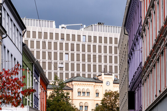 At the end of a corridor, a clock building anchors the view from a street in Oslo, Norway, where historic facades lead toward layered modern architecture in perspective.