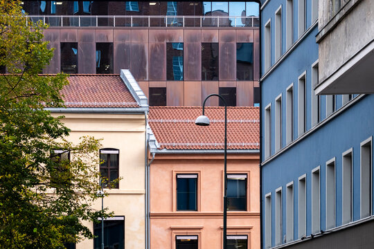 Between tightly framed buildings, a tiled rooftop adds color along a street in Oslo, Norway, where historic facades overlap layered modern architecture.