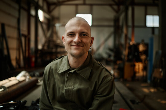 Portrait of young adult Caucasian male welder smiling in industrial workshop. Image represents blue collar workforce and is suitable for manufacturing recruitment campaigns
