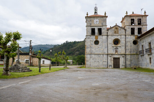 Historic stone facade and towers of San Salvador de Cornellana Monastery with an ancient stone cross in the courtyard, along the Camino Primitivo in Asturias, Northern Spain.