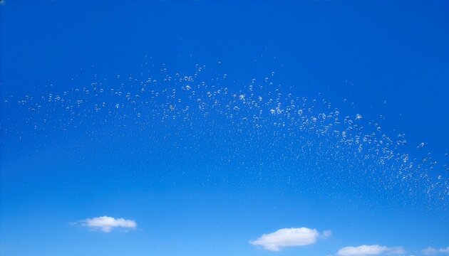 青空と白い雲を背景に弧を描いて舞い散る噴水の水滴と水しぶき　Water Droplets and Splashes Forming an Arc Against a Blue Sky with Clouds