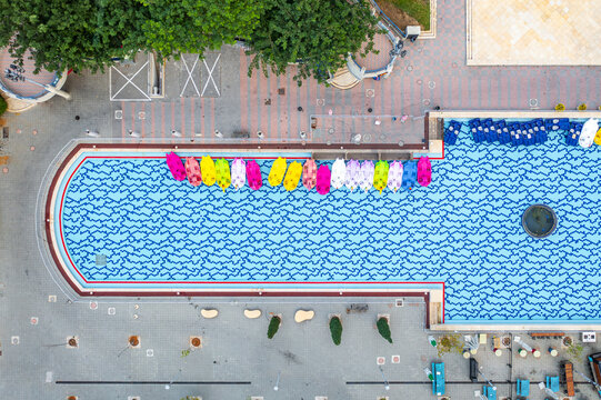 Aerial view of Shimon Peres Park featuring a large pool with a patterned blue surface and colorful pedal boats docked along the edge, surrounded by walkways, Holon, Center District, Israel.