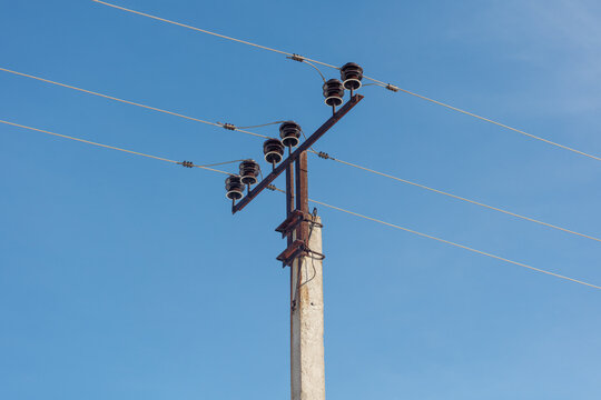 A clear blue sky above a concrete pole. Several wires are strung through the frame. Insulators secure the lines to the pole.