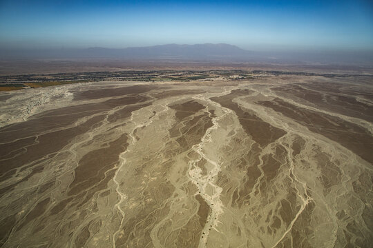 Aerial view of the Nazca Lines, showing the intricate geoglyphs etched into the arid desert landscape, with distant mountains in Nazca Province, Ica, Peru.