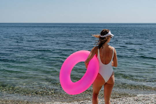 Coastal vacation getaway featuring young woman holding pink swim ring by serene sea shore