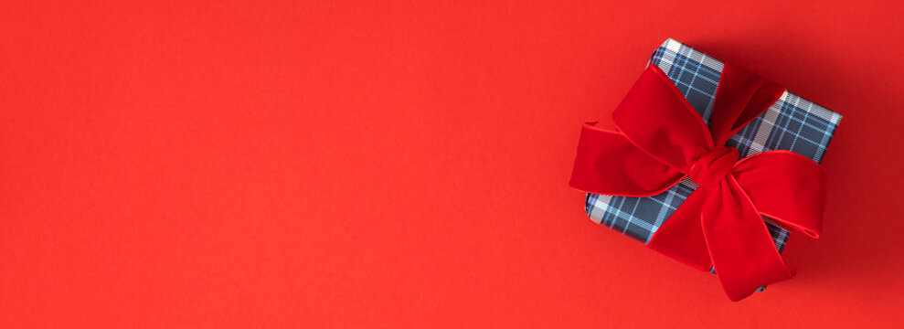 Christmas Gift Box with Red Velvet Ribbon Bow on Red Background Panoramic Banner. Plaid Present Side Border Flat Lay with Copy Space. Minimalist New Year, Holiday Greeting Card Mockup Concept.