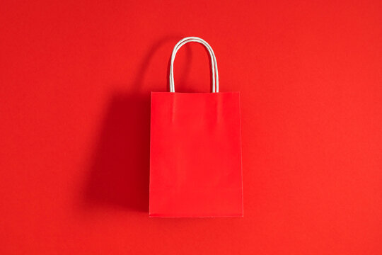 Red Paper Shopping Bag Flat Lay on Vibrant Red Background with Copy Space. Minimalist Retail Craft Present Bag with Handles Top View. Black Friday, Valentine Day Sale and Commercial Mockup Concept.